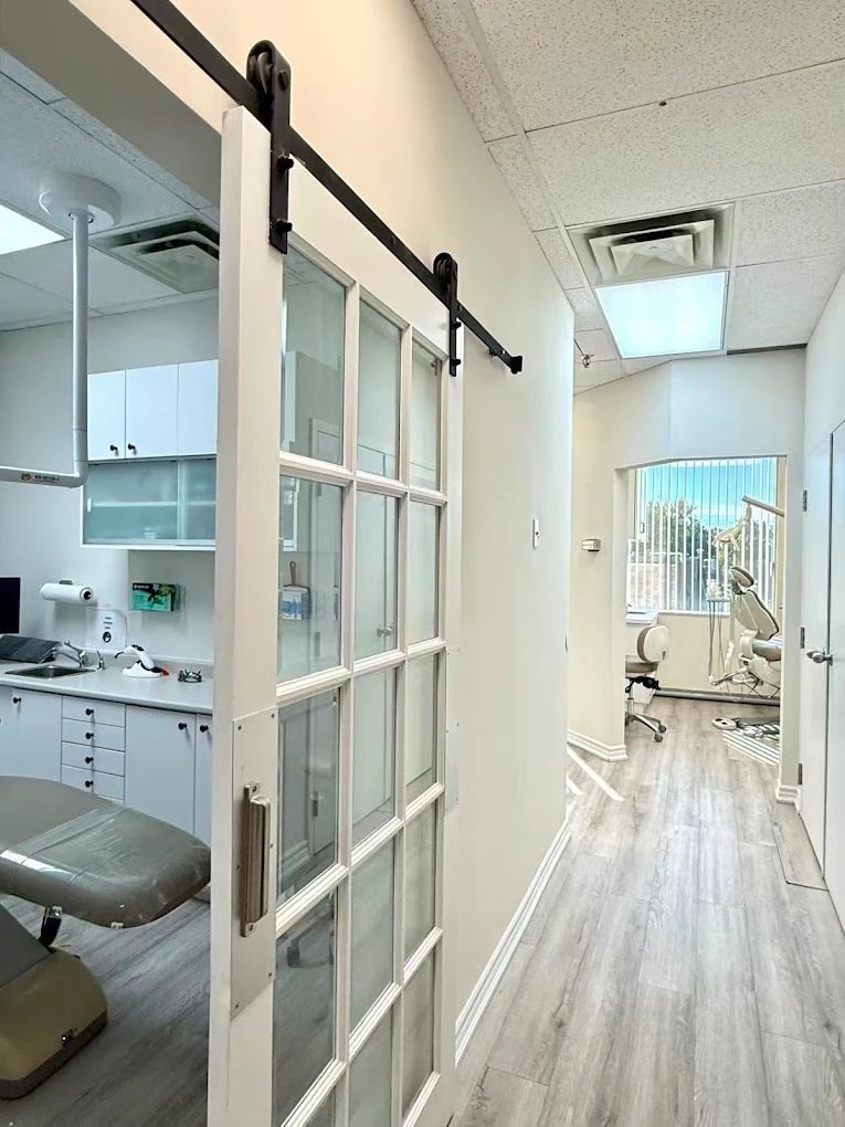 Hallway at Highway 7 Emergency Dental, with a sliding glass door to one treatment room and a dental chair by the window at the end